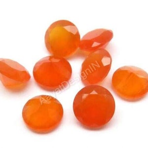 May include: A group of eight orange carnelian gemstones, each with a faceted, round shape. The stones are arranged in a cluster on a white background.