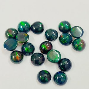 May include: A collection of 16 round, black opal cabochons with green and red flashes. The cabochons are approximately 6mm in diameter.