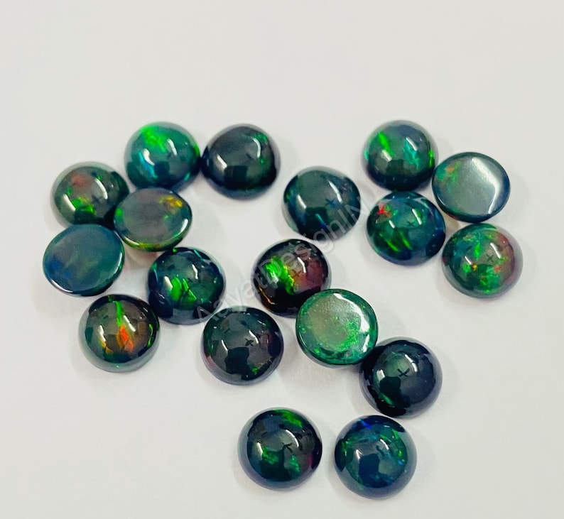 May include: A collection of 16 round, black opal cabochons with green and red flashes. The cabochons are approximately 6mm in diameter.