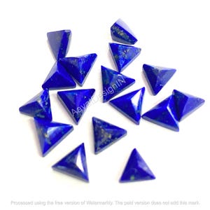 Puede incluir: Un conjunto de gemas triangulares de lapislázuli azul oscuro. Cada piedra está tallada en forma de triángulo perfecto, con motas doradas visibles. Las gemas están dispersas sobre una superficie blanca. El texto "AayatDesignIN" es visible.