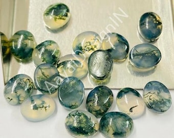 Op de afbeelding: Een verzameling van 15 ovale mosagaat-cabochons. De stenen zijn doorschijnend en hebben een lichtgroene en witte kleur met donkergroene, mosachtige insluitsels.