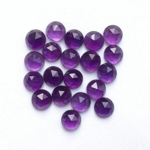 May include: A collection of 20 faceted amethyst gemstones, each with a round shape and a purple hue. The stones are arranged in a loose pile on a white background.