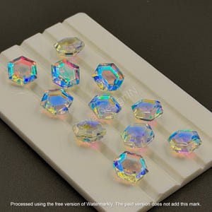 May include: Iridescent, hexagonal crystal beads in various colors, arranged on a white, grooved surface. The crystals reflect light, displaying a spectrum of colors. The image includes the text "KayaksesignIN".