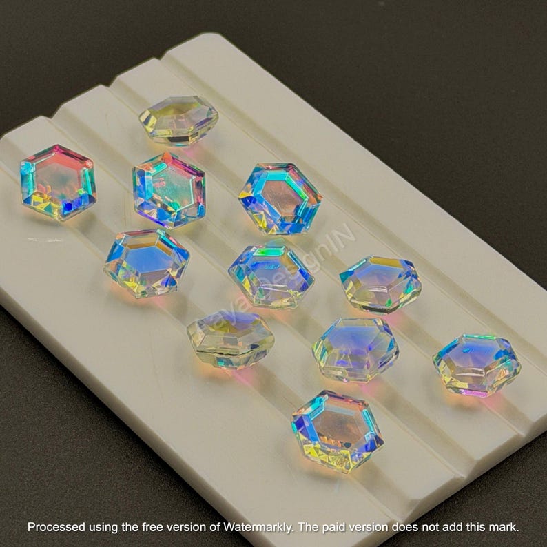 May include: Iridescent, hexagonal crystal beads in various colors, arranged on a white, grooved surface. The crystals reflect light, displaying a spectrum of colors. The image includes the text "KayaksesignIN".