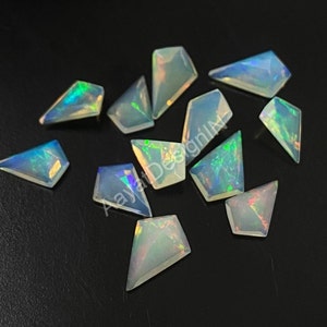 May include: A collection of 12 iridescent white opal gemstone chips in a kite shape. The chips are scattered on a black surface.