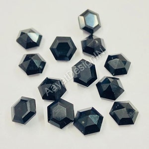 May include: A group of 12 black faceted hexagon shaped gemstones. The gemstones are scattered on a white surface.