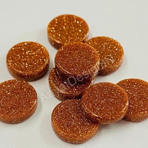 Può includere: Una collezione di otto cabochon rotondi e piatti in pietra di sole color marrone dorato. Le pietre hanno una texture scintillante e brillante.
