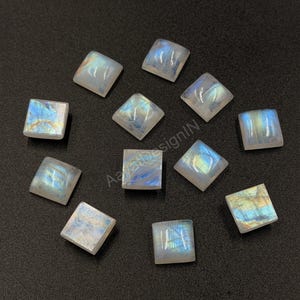 May include: Eleven square-shaped moonstone cabochons with a smooth, polished surface. Each stone displays a translucent white base with iridescent blue and yellow flashes of light. The stones are arranged in a scattered pattern.