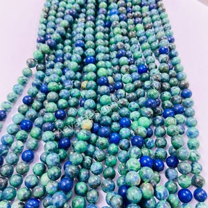 May include: A strand of round, green and blue gemstone beads. The beads are a mix of light and dark green with blue flecks throughout.