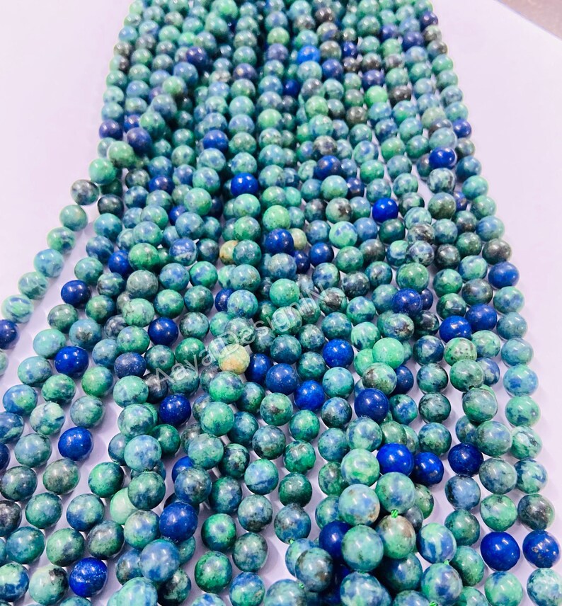 May include: A strand of round, green and blue gemstone beads. The beads are a mix of light and dark green with blue flecks throughout.