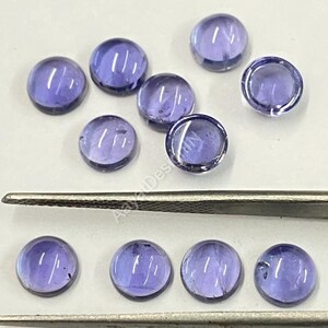 May include: Ten round, purple amethyst cabochons, some with a slight shimmer, arranged in two rows on a white surface. The cabochons are approximately 10mm in diameter.