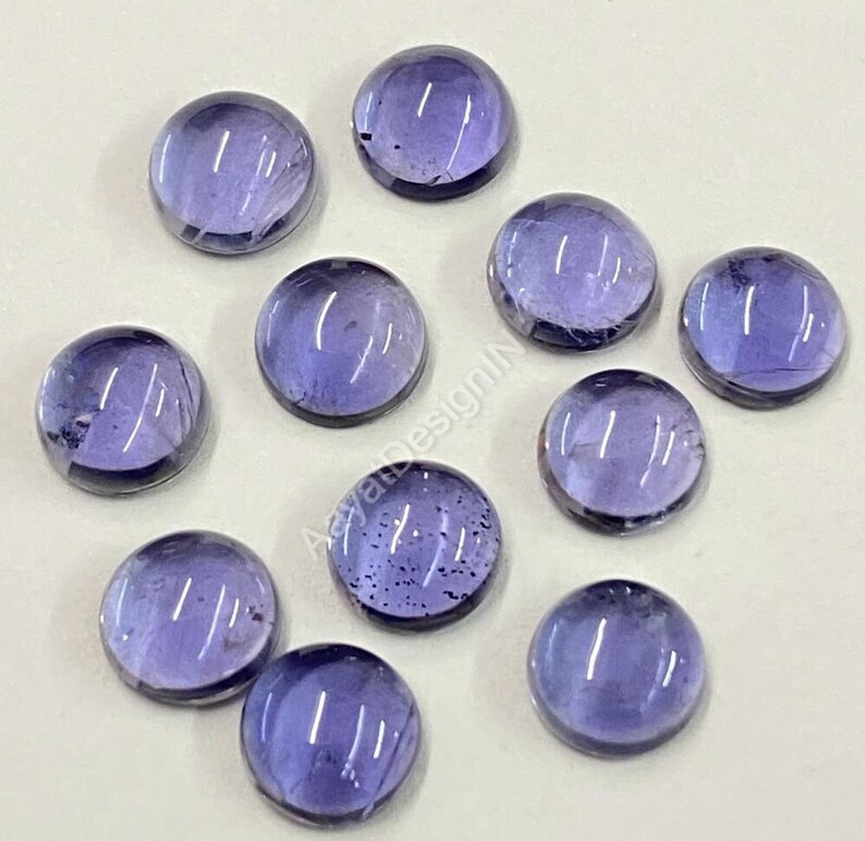 May include: Ten round, smooth, purple gemstones with a slight sheen. The gemstones are approximately 1 cm in diameter.