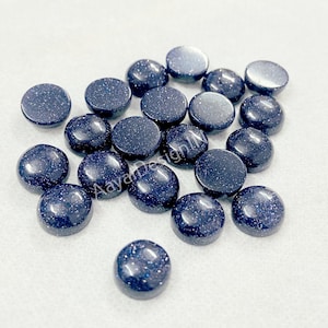 May include: A collection of 18 round, blue, sparkly cabochons. The cabochons are made of blue sandstone and have a speckled appearance.