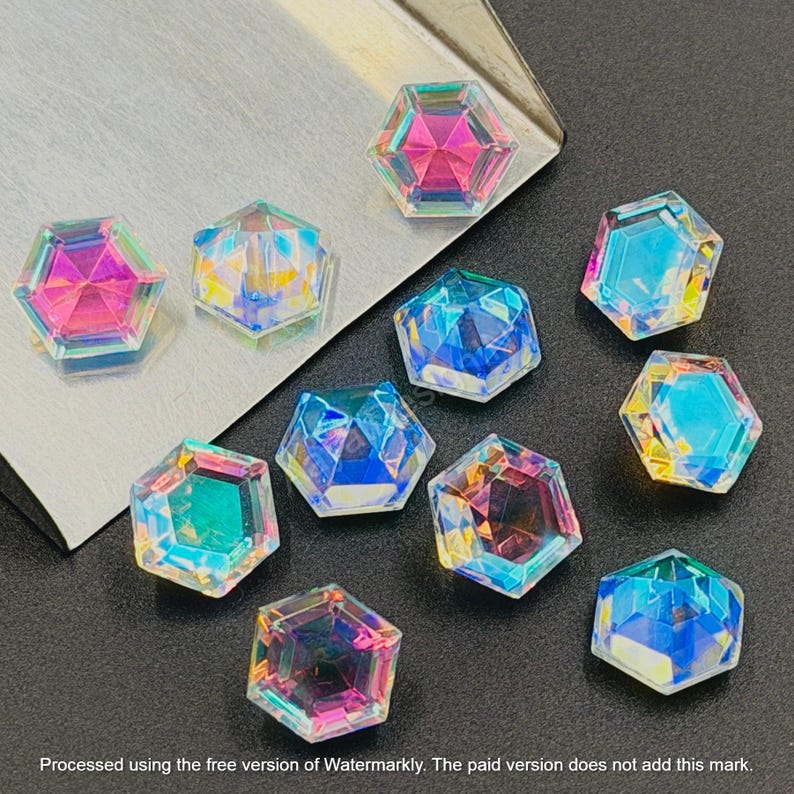 May include: A collection of iridescent, hexagonal-shaped beads. The beads display a spectrum of colors, including pink, blue, and yellow, reflecting light. They are arranged on a dark surface with a silver tray in the background. The image text says: Processed using the free version of Watermarkly.