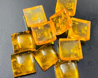 May include: Ten square-shaped amber gemstones with inclusions. The gemstones are a deep orange color and have a glossy finish.