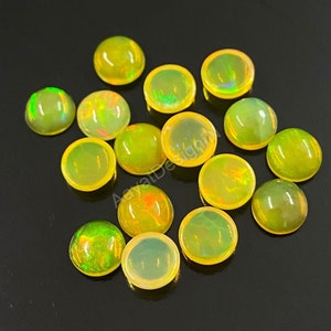 May include: A collection of 14 round, yellow opal cabochons. The cabochons are smooth and have a slight iridescent sheen.