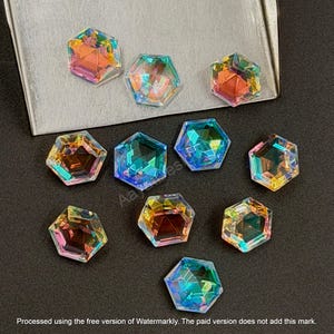 May include: A collection of iridescent, hexagonal crystals in various colors, including orange, green, and blue. The crystals are arranged on a dark surface, with some placed on a silver tray. The image includes text at the bottom.