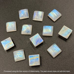 May include: A collection of eleven square-shaped moonstone cabochons, each featuring a smooth, polished surface with a translucent white base and iridescent blue and yellow light reflections that shift across the stones.