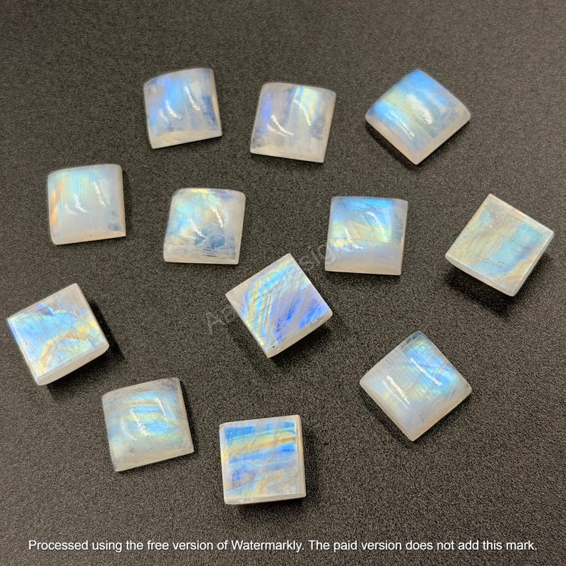 May include: A collection of eleven square-shaped moonstone cabochons, each featuring a smooth, polished surface with a translucent white base and iridescent blue and yellow light reflections that shift across the stones.