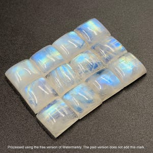 May include: A collection of twelve square-cut moonstone cabochons arranged in a grid. Each translucent stone features a smooth, domed surface with a distinct blue adularescence that shifts in light, displaying a milky white base color.
