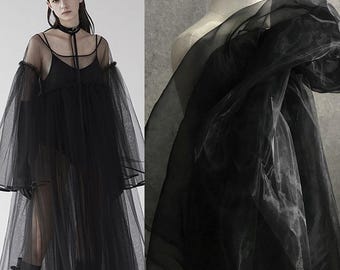 May include: A black sheer dress featuring long voluminous sleeves, a scoop neckline, and a layered tulle skirt. The garment includes a thin black choker strap detail at the neck and is constructed from a translucent, lightweight fabric material.