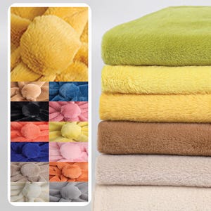 May include: A collection of plush, faux fur fabric in various colors. The image shows a stack of fabric in shades of green, yellow, and brown. A smaller section displays samples in a variety of colors, including blue, pink, and orange. The fabric has a soft, fluffy texture.
