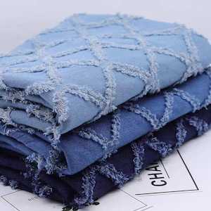 Pode incluir: Uma pilha de tecido jeans em tons de azul. Cada camada apresenta um padrão de diamante criado com bordas desfiadas. O tecido parece macio e tem uma aparência texturizada, adequado para projetos de vestuário ou artesanato.