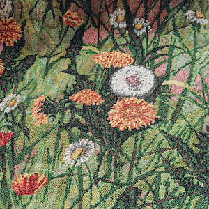 Op de afbeelding: Een wandkleed met een close-up van een bloemenontwerp met rode, witte en gele bloemen. De bloemen zijn in de stof geweven en hebben een textuur.