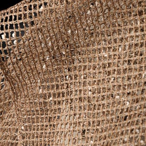 Puede incluir: Primer plano de una tela de malla tejida marr&oacute;n con un patr&oacute;n de cuadr&iacute;cula. La tela tiene una textura ligeramente rugosa y est&aacute; hecha de fibras naturales.