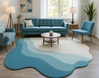 May include: An irregular, organic-shaped area rug featuring layered, wavy bands of color in shades of cream, light blue, and dark teal. The rug has a textured surface and is positioned on a light wood floor in a living room setting.