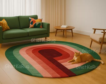 May include: An oval area rug featuring concentric bands of dark green, light green, salmon pink, and deep burgundy. The rug is placed on a light wood floor in a room with a green sofa, a wooden coffee table, and an orange tabby cat resting on it.