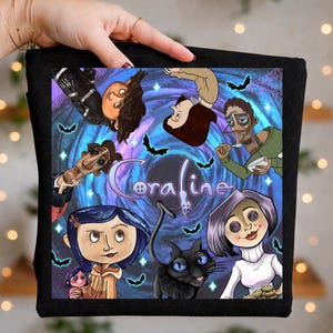 Può includere: Un articolo in tessuto nero con una stampa grafica colorata di personaggi di Coraline, tra cui una ragazza con i capelli blu, un gatto nero e altre figure che circondano la parola Coraline in un vortice blu e viola con piccoli pipistrelli.