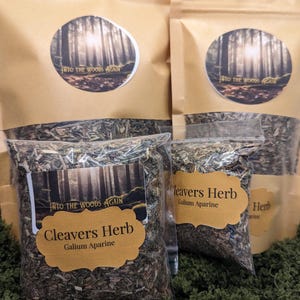 May include: Three brown paper bags with a white logo that says "Into the Woods Again". The bags contain dried herbs labelled "Cleavers Herb Galium Aparine".