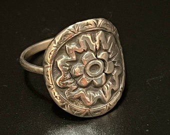 Könnte beinhalten: Ein silberner Ring mit einem floralen Design. Der Ring ist oval geformt und hat ein erhabenes Blumendesign in der Mitte.