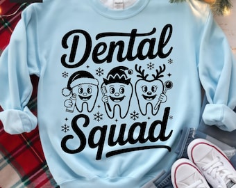 May include: Light blue sweatshirt with the words "Dental Squad" in black script. The design features three cartoon teeth wearing a Santa hat, elf hat, and reindeer antlers, with snowflakes scattered around.