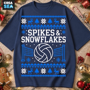May include: A navy blue short-sleeve t-shirt featuring a white graphic print with the text SPIKES & SNOWFLAKES. The design includes a volleyball, volleyball nets, reindeer, pine trees, and snowflake patterns in a festive knit-style layout.