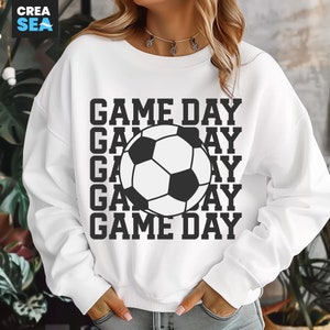 May include: White sweatshirt with a black and white soccer ball graphic and the words "GAME DAY" repeated vertically. The sweatshirt is a casual style, suitable for sports fans.