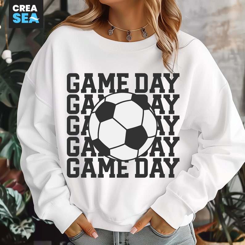 May include: White sweatshirt with a black and white soccer ball graphic and the words "GAME DAY" repeated vertically. The sweatshirt is a casual style, suitable for sports fans.