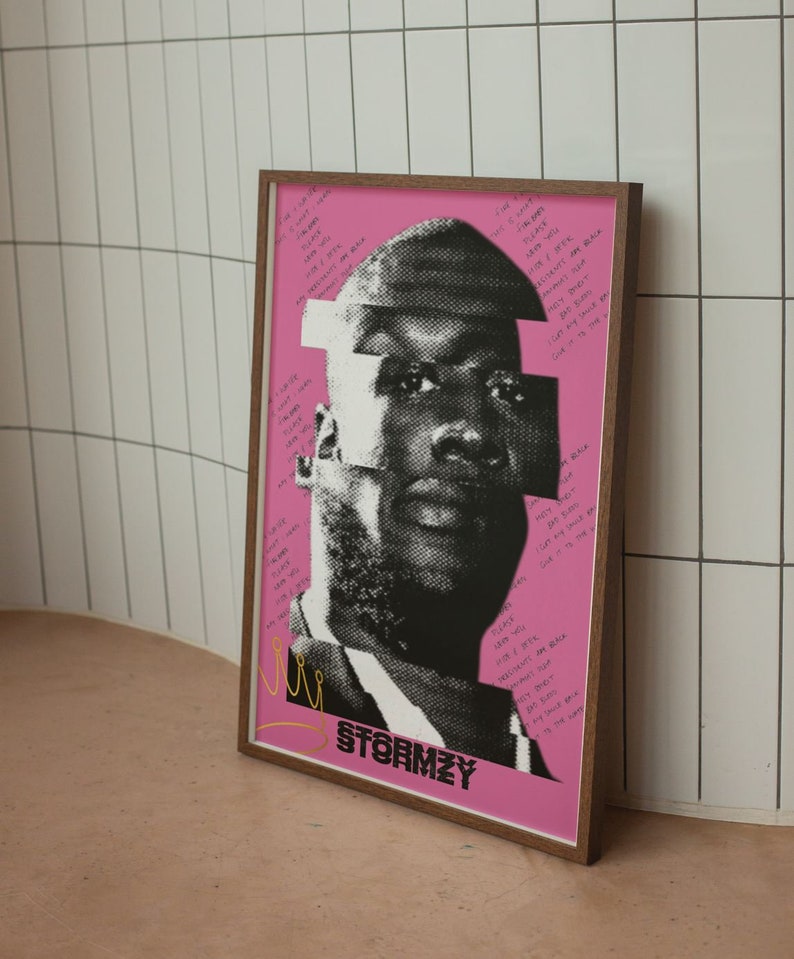 May include: A framed poster featuring a black and white portrait of a man with a pink background. The image has a fragmented design with text and the name "STORMZY" at the bottom. The frame is a warm brown color.