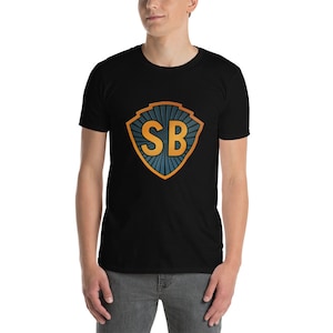 May include: Black t-shirt with a shield design. The shield features the letters "SB" in gold, set against a blue and orange sunburst pattern. The shirt is short-sleeved and made of a soft material.