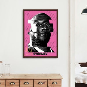 May include: A framed art print featuring a black and white portrait of Stormzy on a pink background. The image has a glitch art style with text elements and a yellow line. The print is in a dark brown frame.