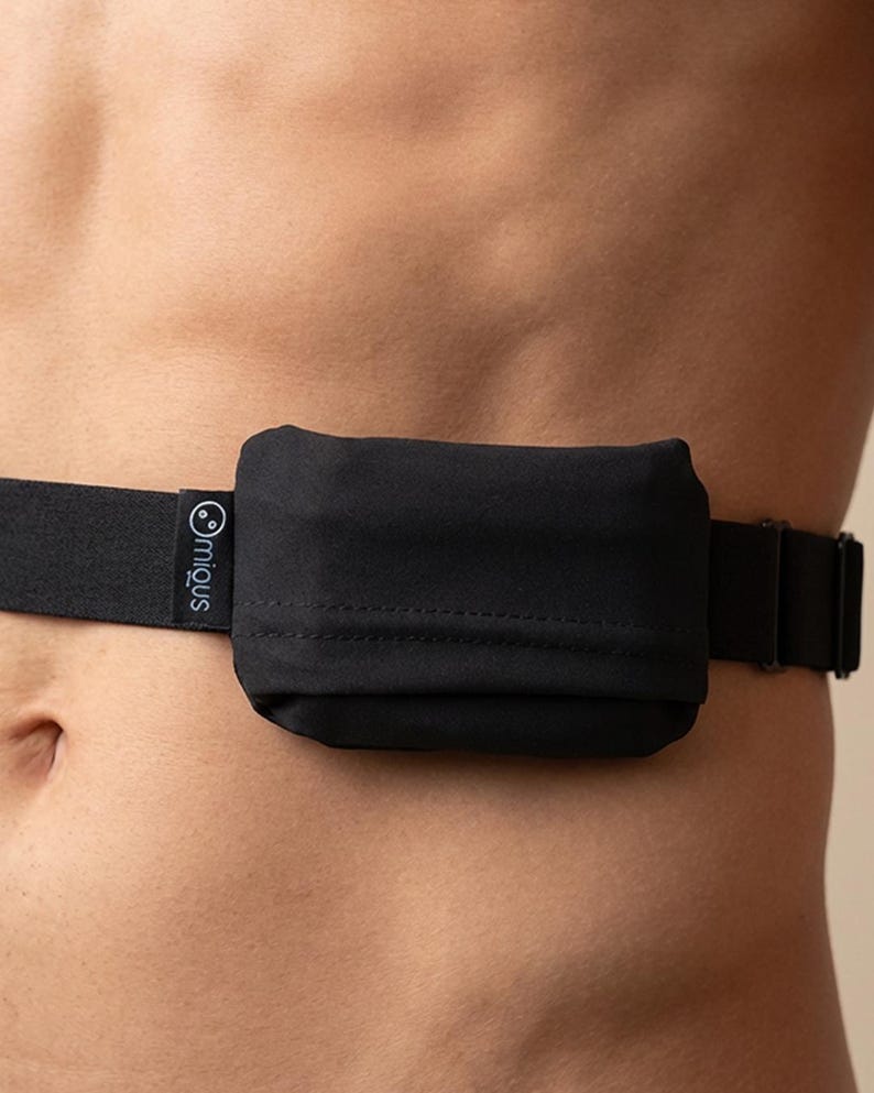 May include: Black waist belt with a small, rectangular pouch. The belt is made of a black elastic material and features a buckle closure. The pouch has a smooth texture and is attached to the belt. The brand name "miqus" is printed on the belt.