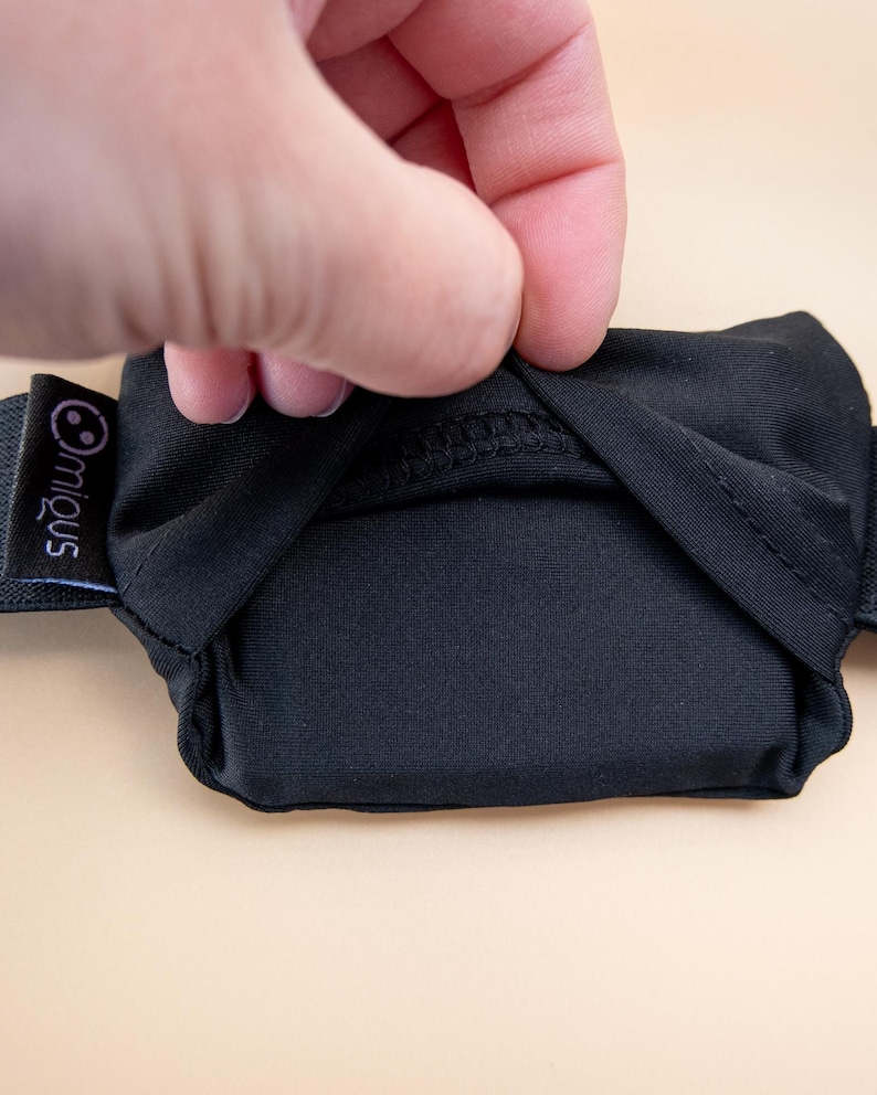 May include: Black eye mask with an elastic band. The mask is made of a soft, opaque material. The brand name "miqous" is printed on a small black tag attached to the elastic band.