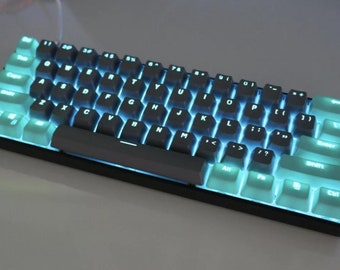 May include: A white and gray mechanical keyboard with a black frame and a teal backlight. The keyboard has a standard layout with function keys, arrow keys, and a number pad.