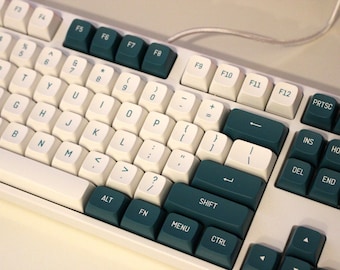 以下が含まれることがあります： 白地にターコイズブルーのキーが付いたキーボード。キーボードは、ファンクションキー、数字キー、アルファベットキーを備えた標準レイアウト。ターコイズブルーのキーは、ファンクションキー、矢印キー、エンターキー、シフトキー、コントロールキー、アルトキー、メニューキー、インサートキー、ホームキー、ページアップキー、削除キー、エンドキー、ページダウンキー、プリントスクリーンキー用です。