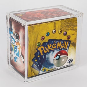 Può includere: Una teca in acrilico trasparente sigillata contenente un box di bustine di carte collezionabili Pokemon. La confezione gialla presenta il logo Pokemon, una Poke Ball rossa e bianca e la scritta 1st Edition Limited Printing sul davanti.