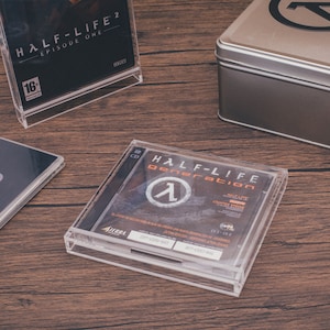 Könnte beinhalten: Ein transparentes Plastikgehäuse mit einer CD darin. Die CD ist mit "HALF-LIFE generation" beschriftet und zeigt das Half-Life-Logo. Das Gehäuse befindet sich auf einer Holzoberfläche.
