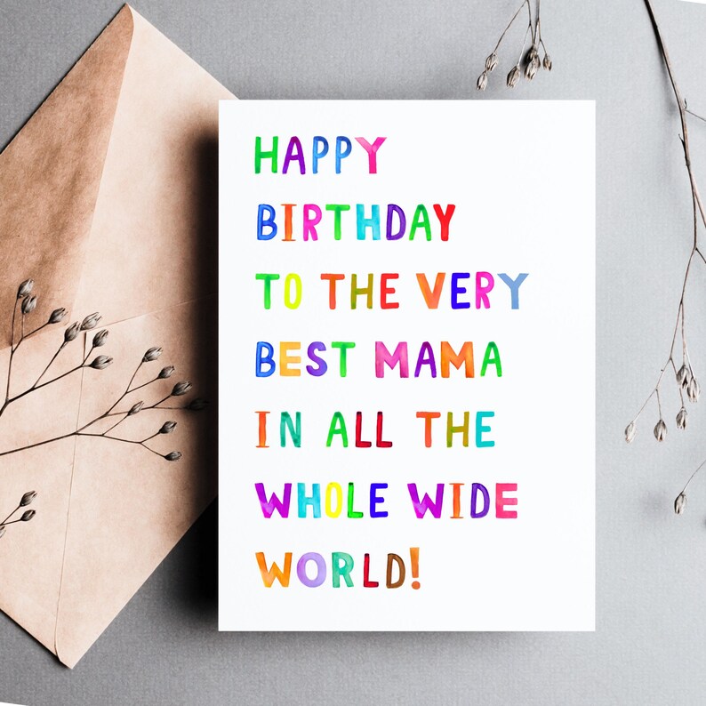 May include: A white birthday card with the text "HAPPY BIRTHDAY TO THE VERY BEST MAMA IN ALL THE WHOLE WIDE WORLD!" in colorful, watercolor-style lettering. The card is next to a brown envelope and sprigs of greenery.