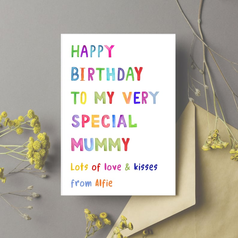 May include: A white birthday card with colorful text that reads "HAPPY BIRTHDAY TO MY VERY SPECIAL MUMMY." The card includes the message "Lots of love & kisses from Alfie." The card is next to a brown envelope and yellow flowers.