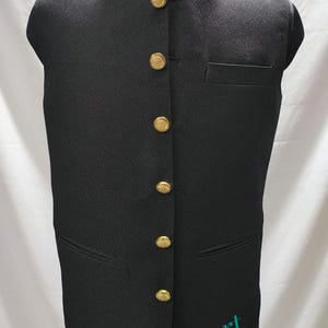 Puede incluir: Un chaleco negro sin mangas con cuello mandar&iacute;n y botones dorados. El chaleco tiene un bolsillo en el lado derecho y el texto "Sifatart" est&aacute; impreso en la parte inferior.